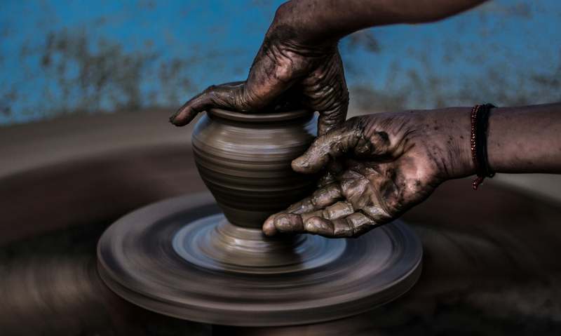 Close-up of hands centering wet clay on a white pottery wheel, with subtle ceramic tools in soft focus background